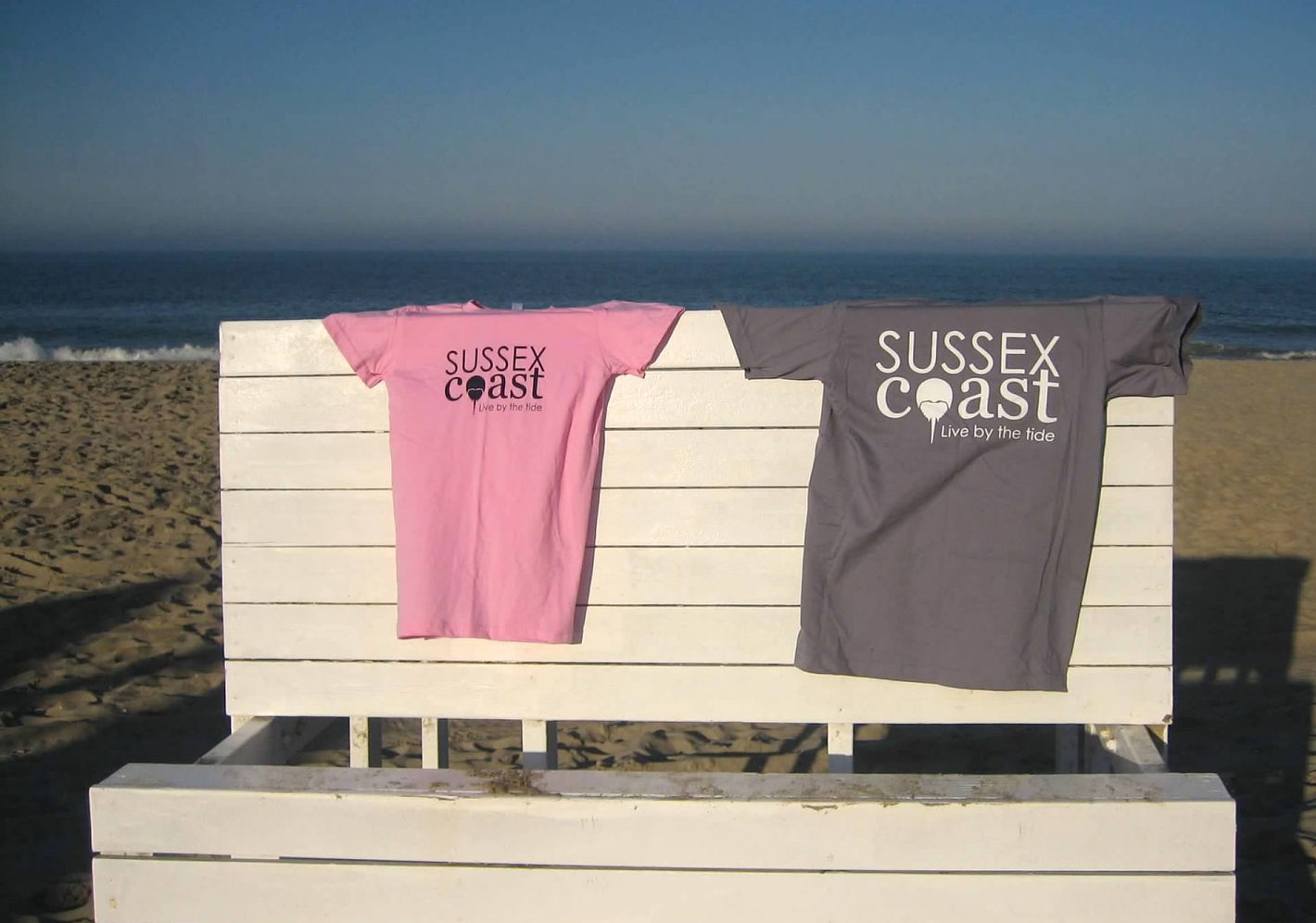 Pink and grey Sussex Coast t-shirts draped on lifeguard stand in Bethany Beach